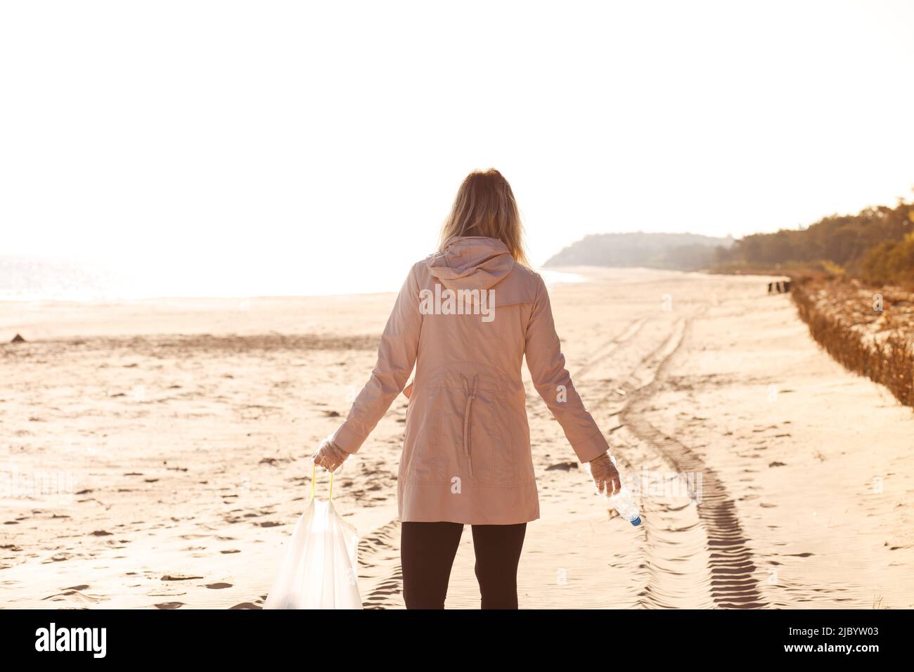 Rückansicht einer Freiwilligen, die am Strand steht und Flasche, Reinigungsbereich und Meer vor Plastikmüll hält. Speicherplatz kopieren Stockfoto