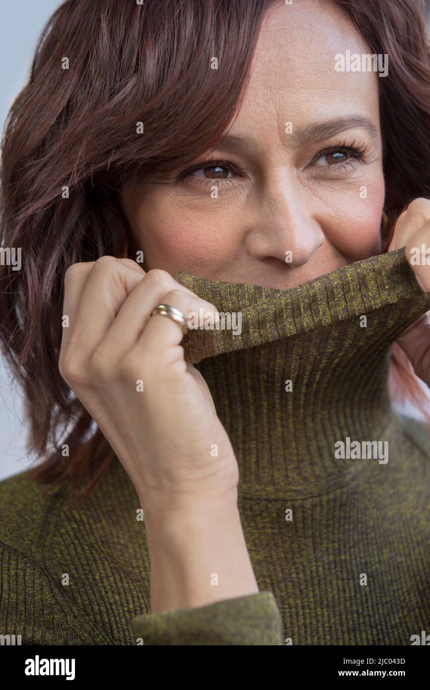 Nahaufnahme einer Frau mit rotem Kopf mittleren Alters, die ihr Gesicht mit ihrem Rollkragen-Pullover bedeckt. Stockfoto