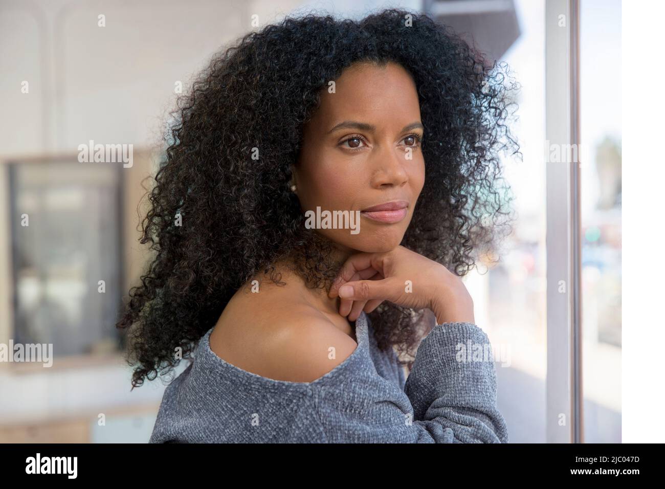 Eine Frau mittleren Alters blickt aus einem Fenster mit der Hand unter ihrem Kinn. Stockfoto