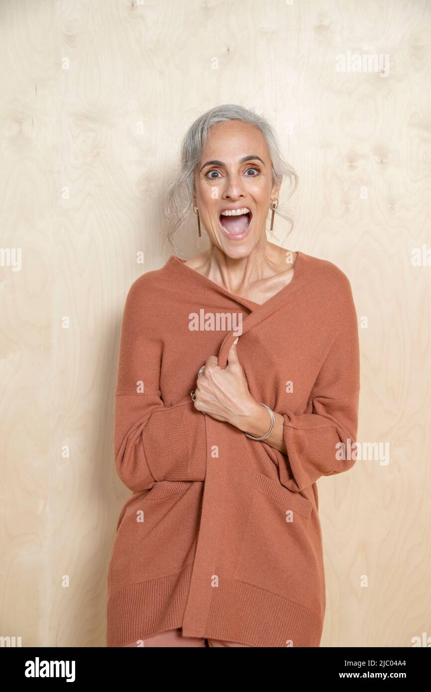 Eine junge Frau mittleren Alters schließt ihren Pullover und lacht vor der Kamera. Stockfoto