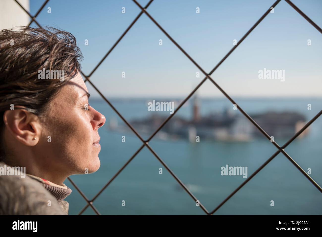 Woman Joy der Panoramablick über die Insel San Giorgio Maggiore hinter einem Metallgitter in Venedig, Venetien in Italien. Stockfoto