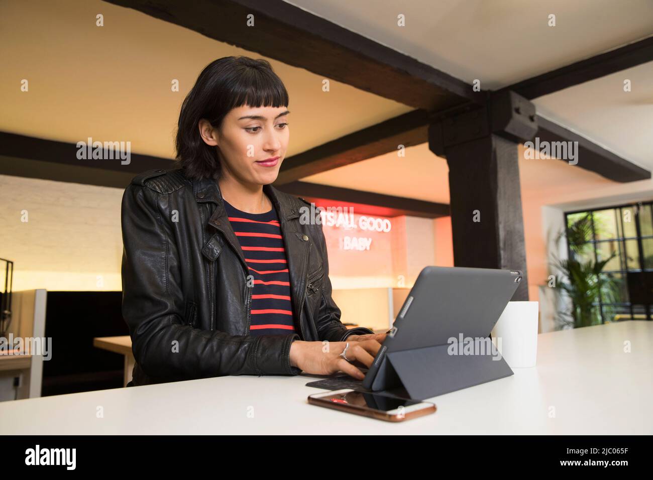 Frau, die an der Theke sitzt und auf einem Tablet im Co-Working-Bereich arbeitet Stockfoto