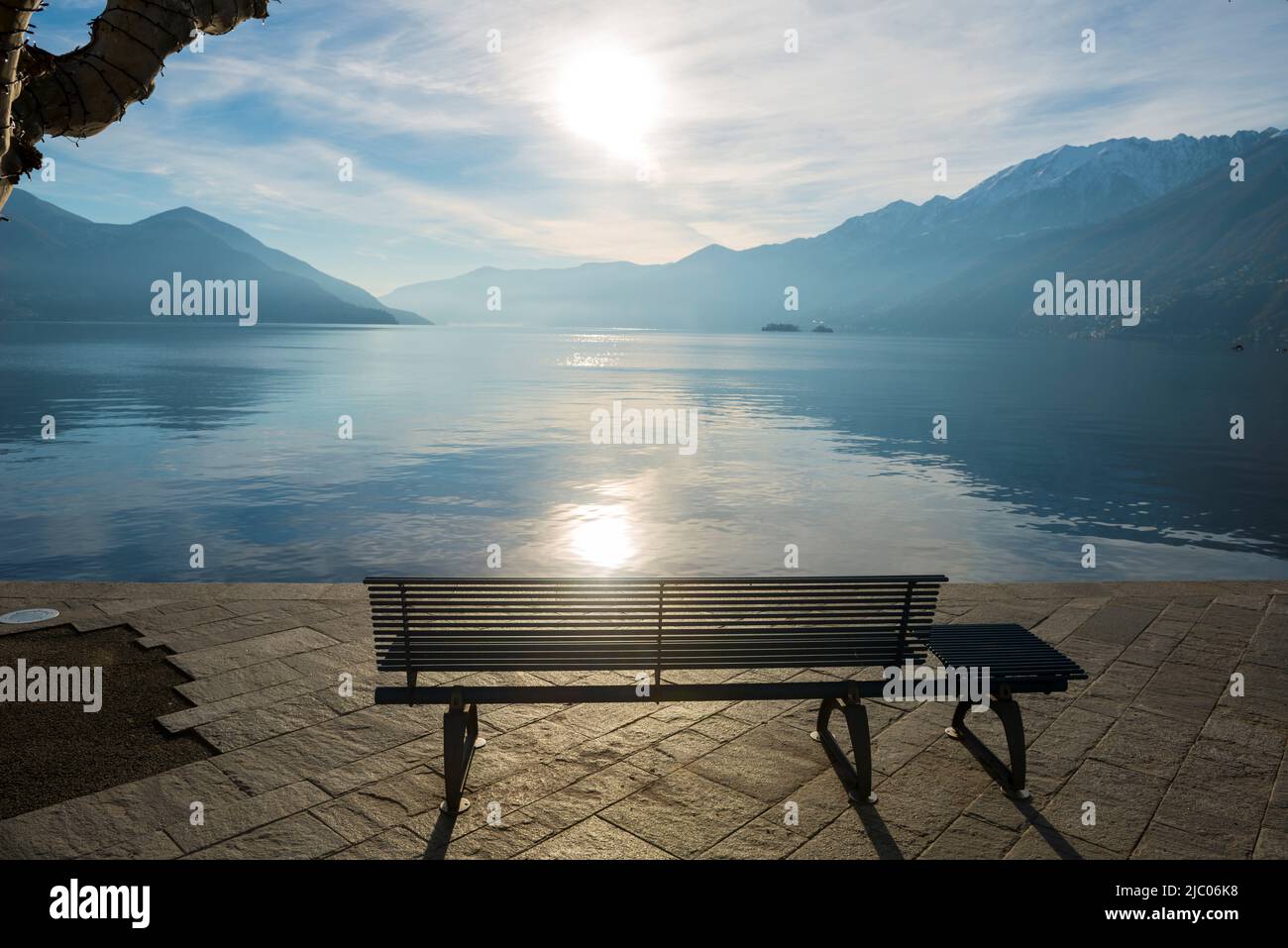 Bank an der Waterfront am Alpinen Lago Maggiore mit Sonnenlicht und Berg in Ascona, Schweiz. Stockfoto