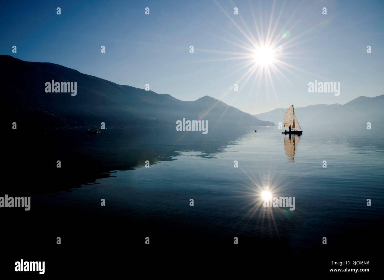Segelschiff auf einem alpinen Lago Maggiore und Berg und reflektiertes Sonnenlicht in Ascona, Schweiz. Stockfoto
