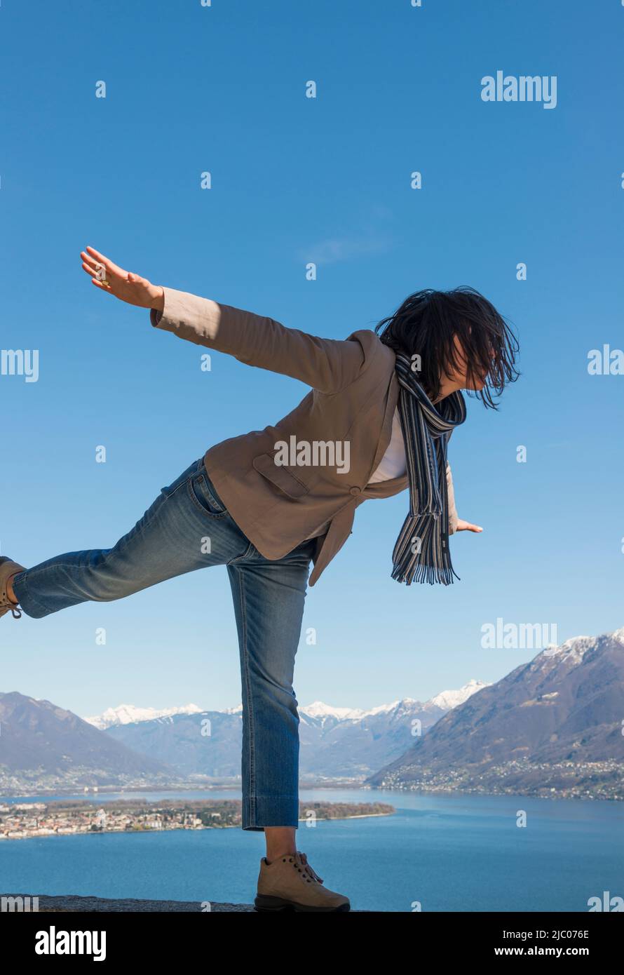 Mit ausgestreckten Armen und auf einem Bein stehend genießen Sie den Panoramablick über den alpinen Lago Maggiore mit schneebedecktem Berg in Ascona, Schweiz. Stockfoto