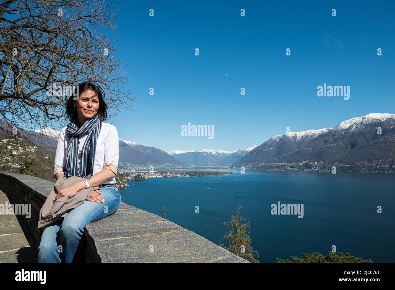 Frau sitzt und genießen Sie den Panoramablick über den Alpensee Maggiore mit schneebedeckten Berg in Ascona, Schweiz. Stockfoto