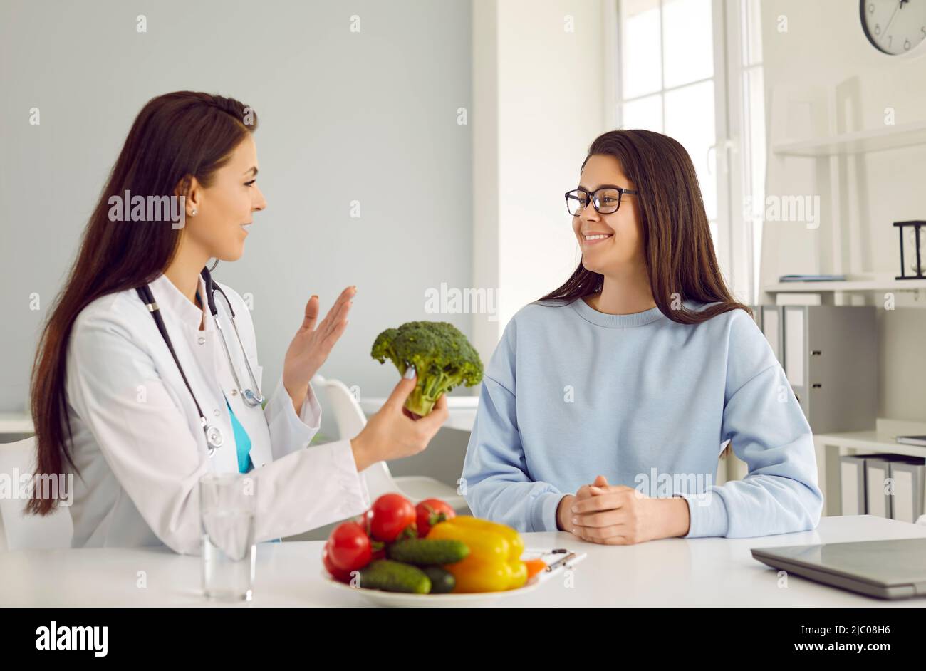 Ernährungsberaterin erzählt der jungen Frau von den Vorteilen des Verzehrs von Gemüse während der Konsultation. Stockfoto