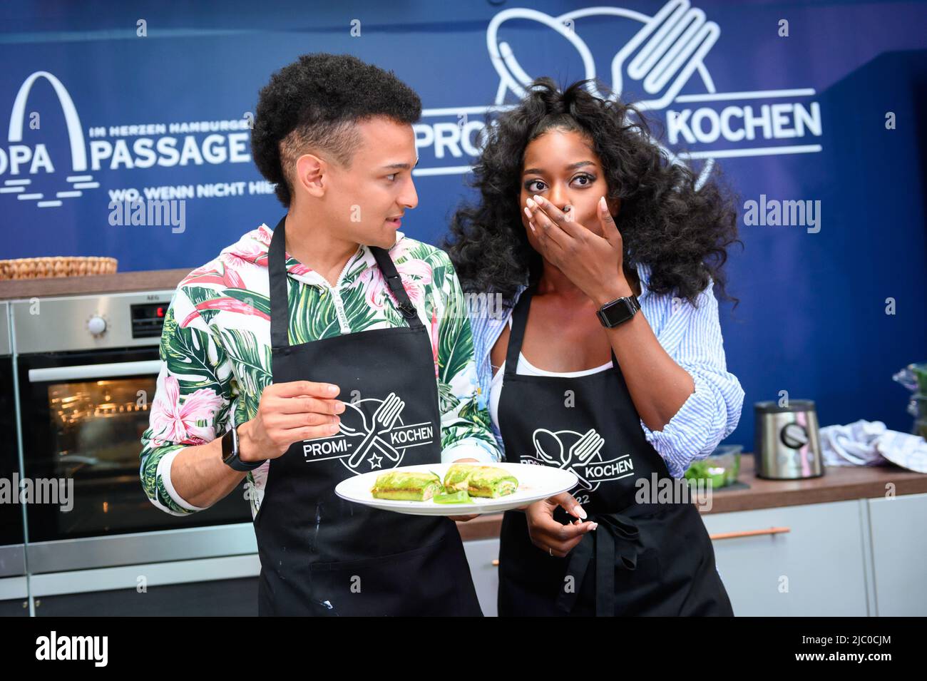 Hamburg, Deutschland. 08.. Juni 2022. Linda Nobat (r), Model, probiert die noch heiße Low Carb Lachsrolle von Prince Damien Ritzinger (l), Sängerin und Musical-Performerin. Um der Hamburger Lebensmittelbank in Not ein wenig zu helfen, findet in der Europa Passage eine Wohltätigkeitsveranstaltung statt. Bis Samstag kochen dort Prominente mittags ihre Lieblingsgerichte für Besucher des Einkaufszentrums. Quelle: Jonas Walzberg/dpa/Alamy Live News Stockfoto
