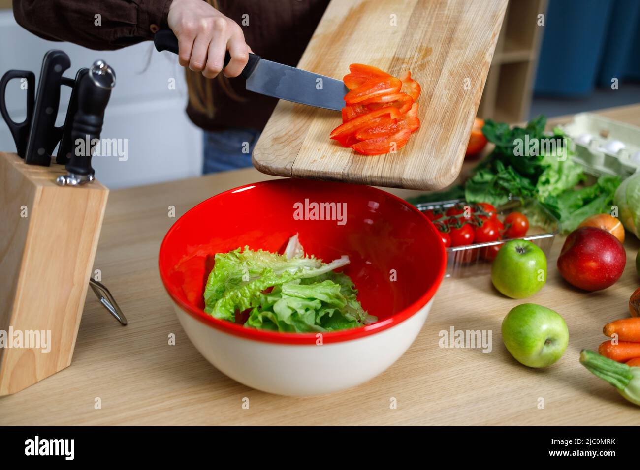 Frau wirft gehackten Pfeffer in die Schüssel. Gesunde Ernährung, vegetarisches Essen, Kochen, Diät-Konzept Stockfoto