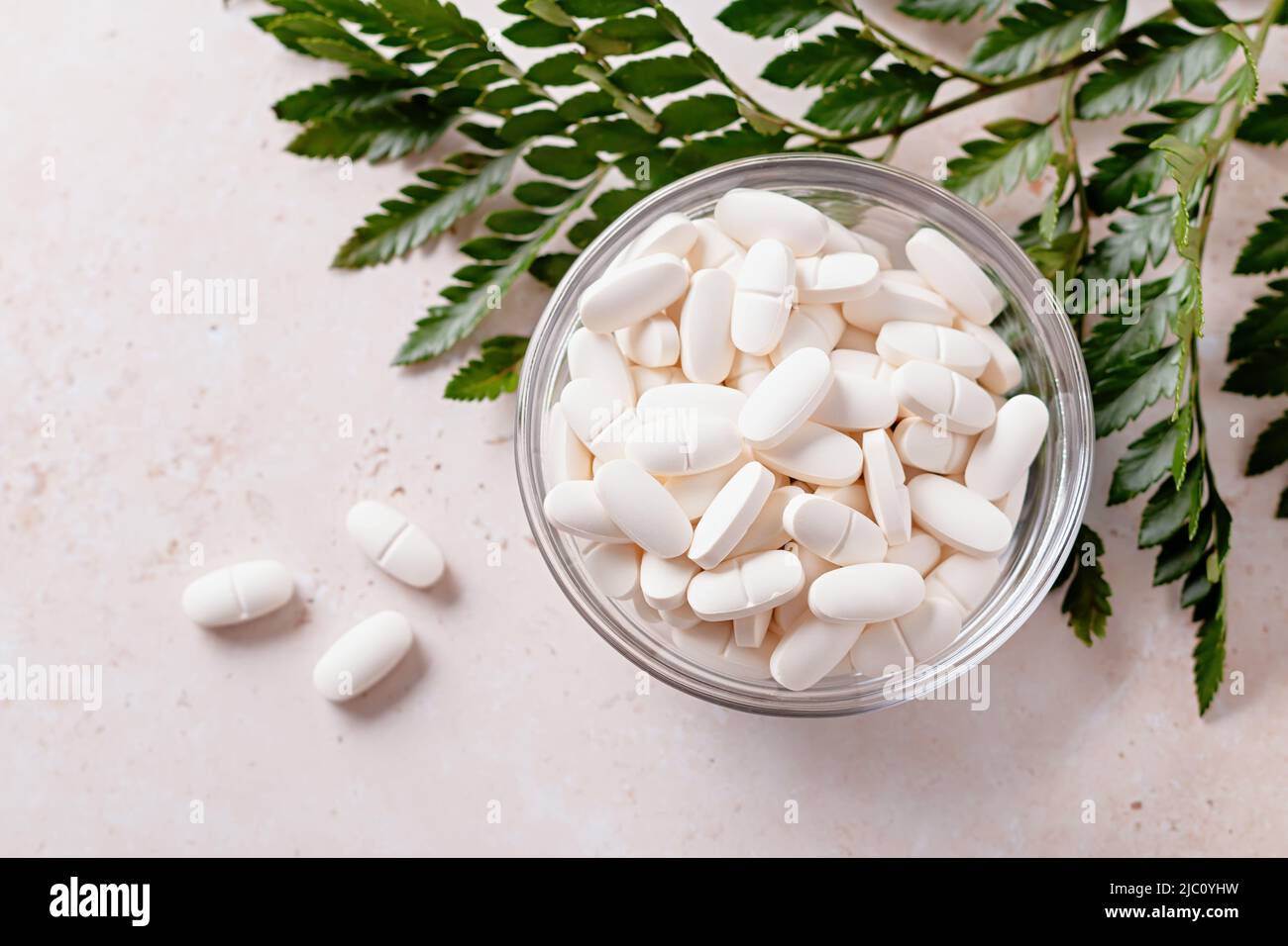 Collagen Pillen und grüne Pflanze auf beigefarbenem Stein Hintergrund, Draufsicht. Kollagen Ergänzung in Pillen für Haut und Gelenke, minimale Zusammensetzung Stockfoto