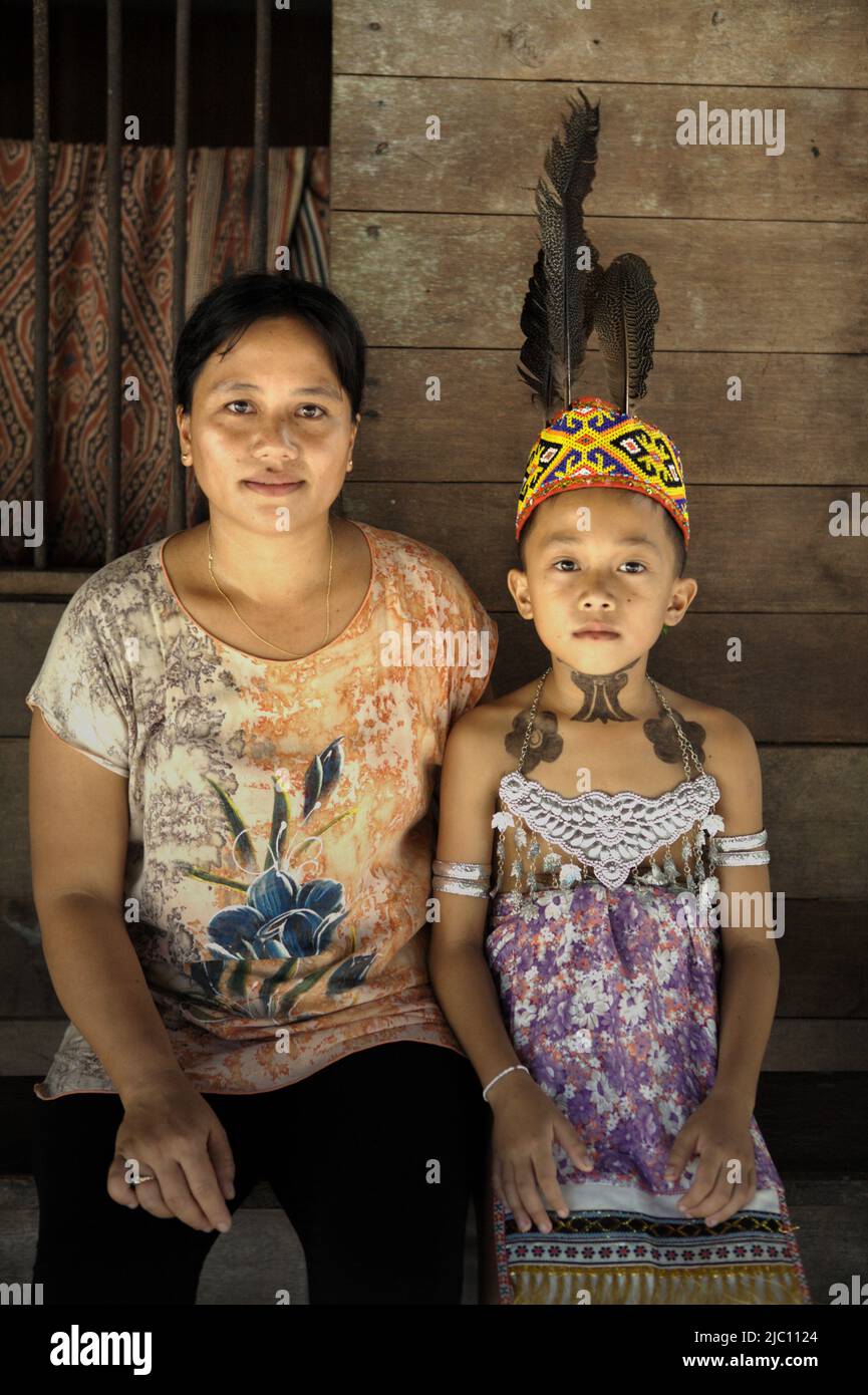 Porträt eines Kindes in traditioneller Kleidung, mit temporären Tattoos mit Marker, während er zusammen mit seiner Mutter sitzt, nachdem er an einer Begrüßungszeremonie während einer Ökotourismus-Veranstaltung im Longhouse der traditionellen Dayak IBAN-Gemeinde in Sungai Utik, Batu Lintang, Embaloh Hulu, Kapuas Hulu, West Kalimantan, Indonesien. Stockfoto