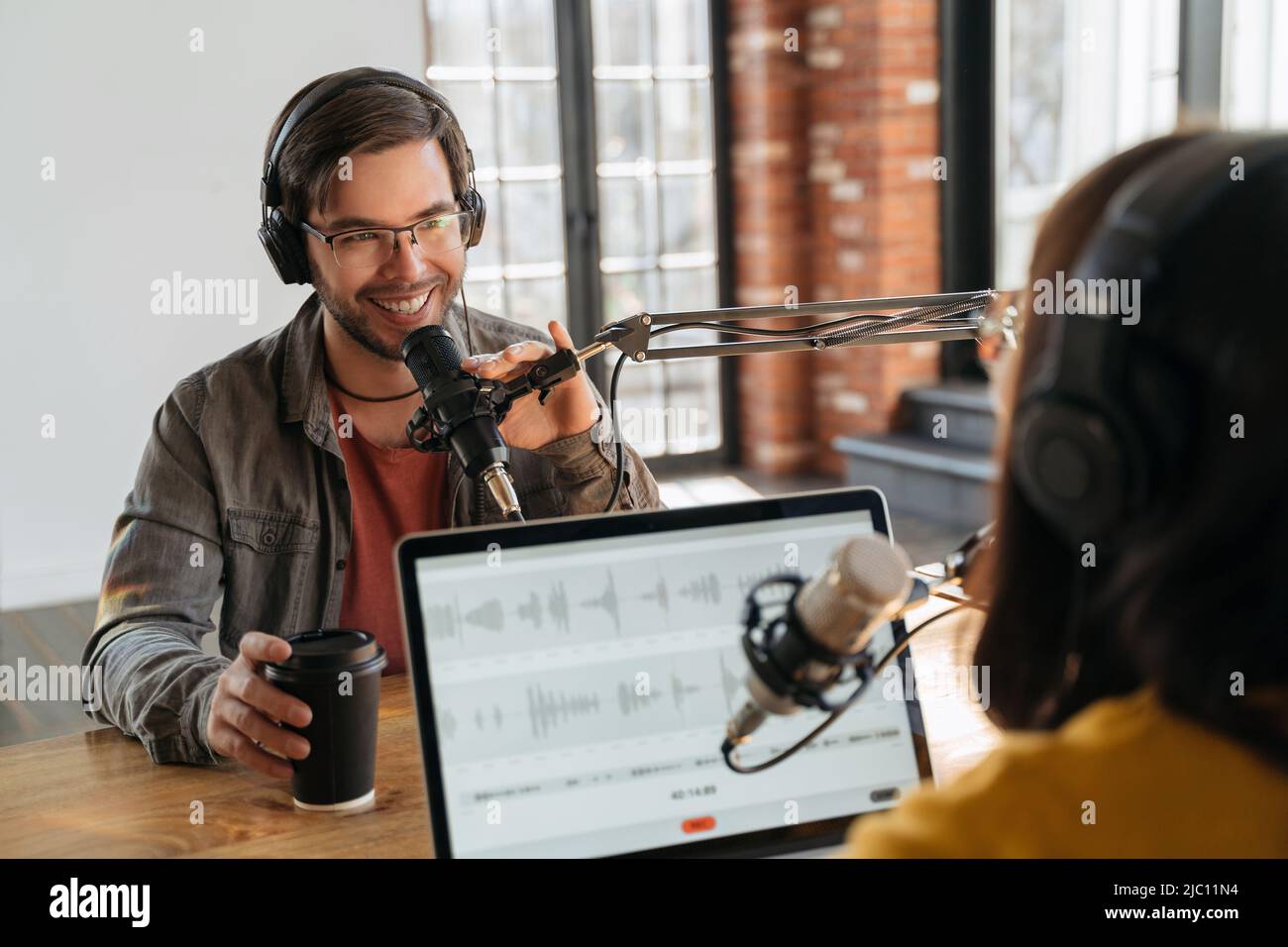 Weibliche Podcast-Kreator interviewten einen gutaussehenden lächelnden männlichen Gast während der Aufnahme Audio-Podcast im Studio. Mann und Frau Podcasters genießen Podcasting, sprechen miteinander, sprechen im Mikrofon Stockfoto