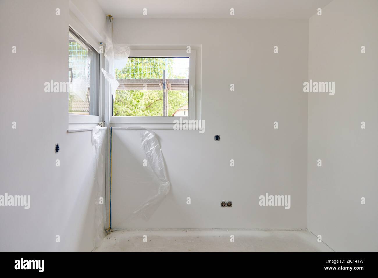Malerarbeiten in einem kleinen Raum mit Eckfenster und weißen Wänden Stockfoto