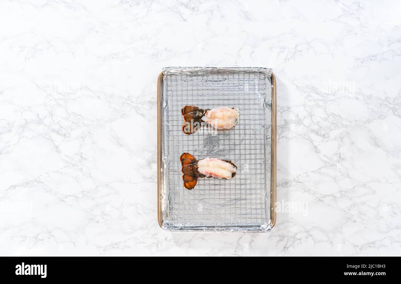 Flach liegend. Rohe Hummerschwänze auf einem Backblech mit Küchenfolie, fertig zum Backen im Ofen. Stockfoto