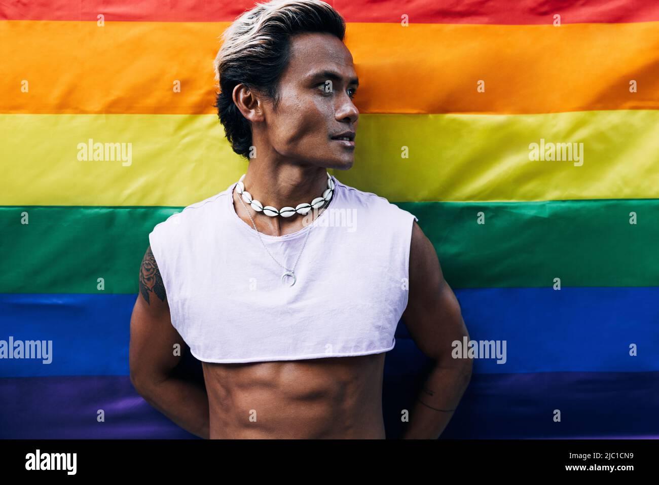 Porträt eines hübschen Mannes, der wegschaut, während er gegen die LGBT-Flagge des Regenbogens steht Stockfoto
