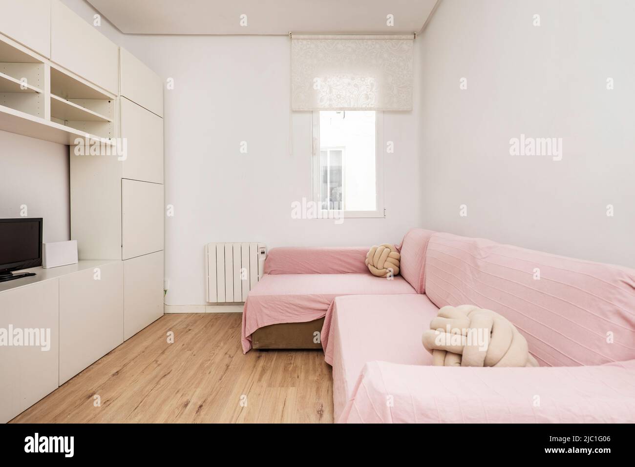 Wohnzimmer eines Ferienhauses mit einem Sofa mit einer Chaiselonge mit rosa Stoffen und einem Bücherregal mit weißen Möbeln und einem hellen Holz bedeckt Stockfoto