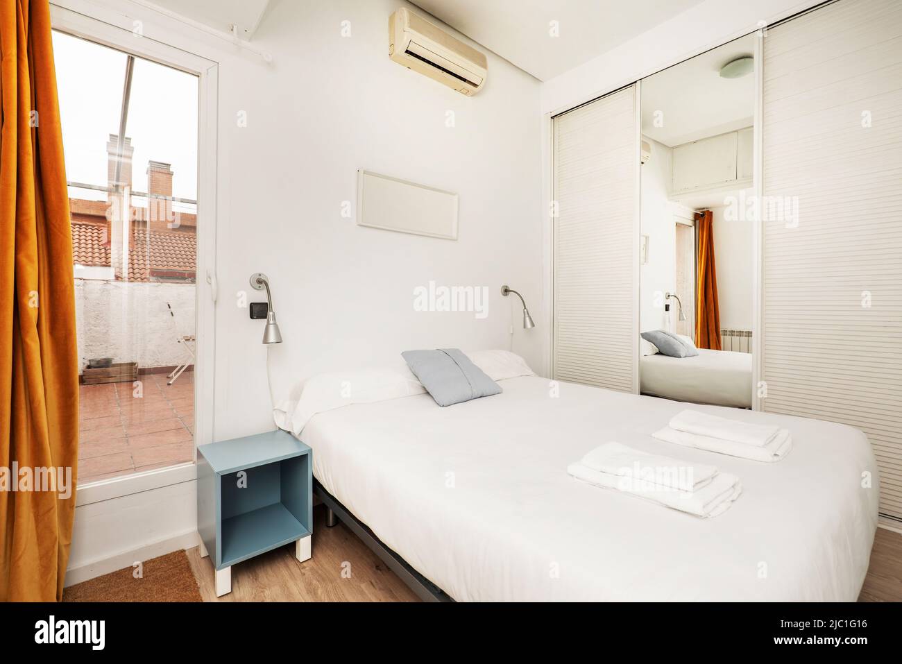 Schlafzimmer mit einem Doppelbett mit einer weißen Tagesdecke, einem Einbauschrank mit weißen Schiebetüren aus venezianischem Holz, einem weiteren mit Spiegel und blauen Betten Stockfoto