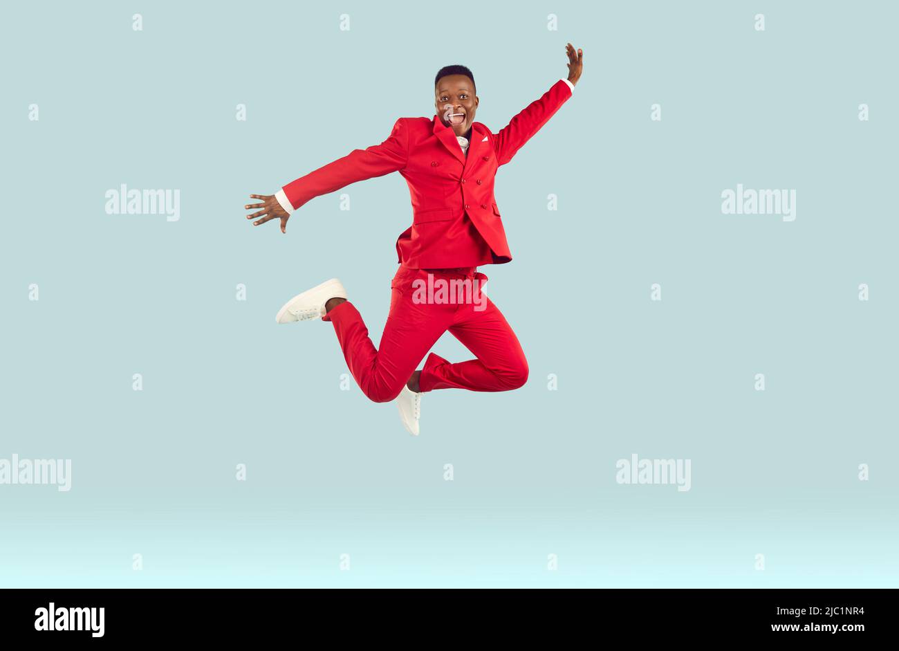 Fröhliche lustige junge afroamerikanische Mann in roten Anzug hohe Sprünge auf pastellfarbenem hellgrauem Hintergrund. Stockfoto