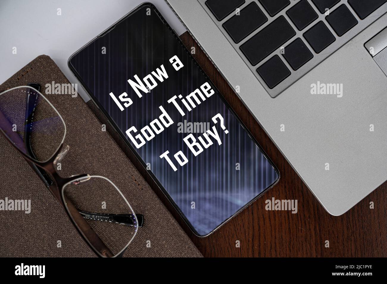 Ist jetzt ein guter Zeitpunkt, um zu kaufen? Ansicht des Telefons auf dem Tisch neben Laptop, Notizblock und Brille mit Aufschrift. Stockfoto