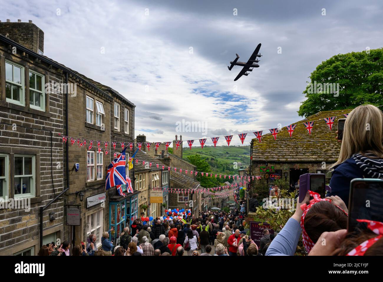 Haworth 1940er-Wochenende (geschäftige, überfüllte Main Street, dekoriert in Union Jacks, beobachten eines historischen Flugzeugs, jährliche Veranstaltung) - West Yorkshire, England, Großbritannien. Stockfoto