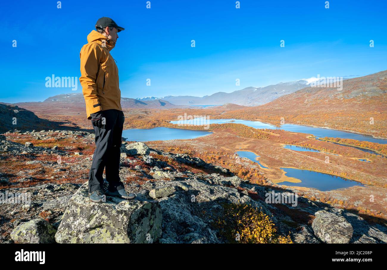 Männlicher Wanderer in gelber Hardshell-Jacke und schwarzer Hose mit Blick auf die gewaltige arktische Landschaft des Stora Sjofallet National Park, Schweden, ON Stockfoto