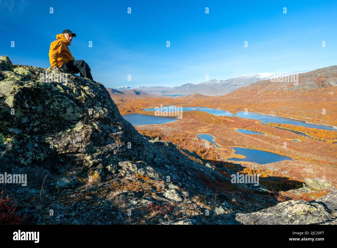 Männlicher Wanderer in gelber Hardshell-Jacke und schwarzer Hose mit Blick auf die gewaltige arktische Landschaft des Stora Sjofallet National Park, Schweden, ON Stockfoto