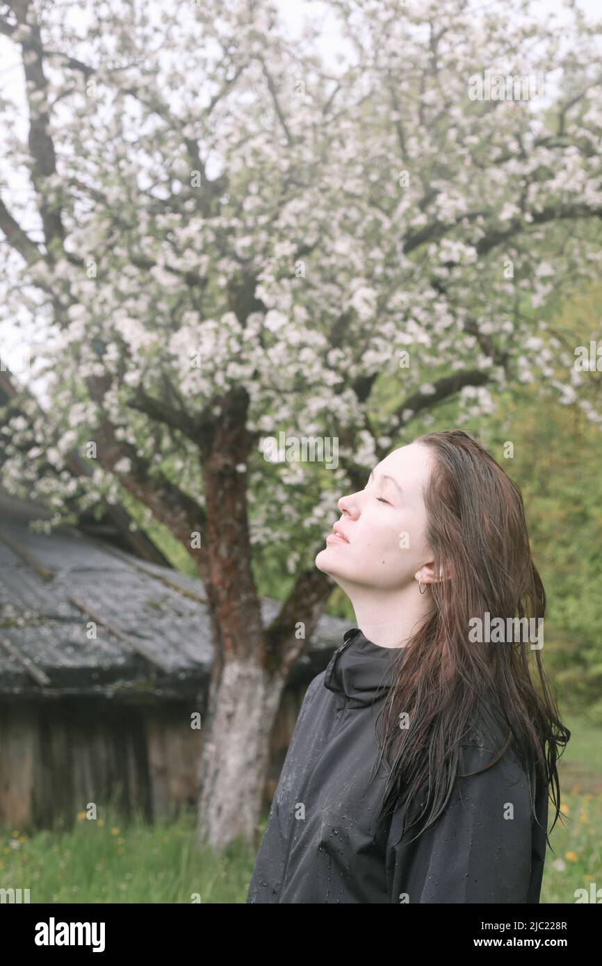 Emotionales Porträt einer jungen Frau, die im Frühling allein unter Regen im Freien steht. Stockfoto