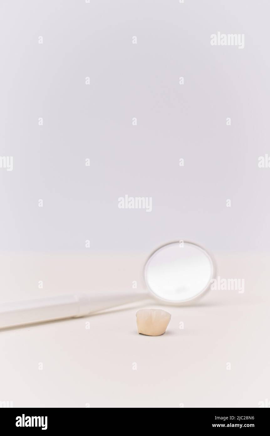 Keramik Zahnkrone Zahnersatz und Zahnspiegel auf einem weichen beigen Schreibtisch - Gesundheitskonzept Stockfoto