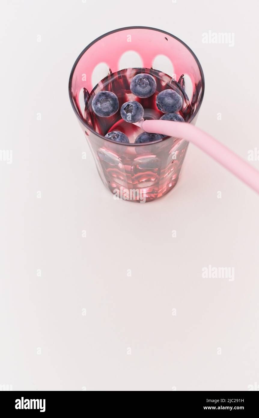 Ein Glas Gin mit Heidelbeeren und Trinkhalm auf einem weichen weißen Tisch Stockfoto