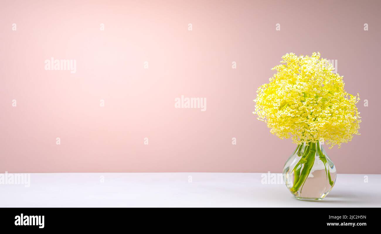 Bouquet von kleinen gelben Blumen in einer Glasvase auf dem Tisch auf einem rosa Hintergrund Stockfoto