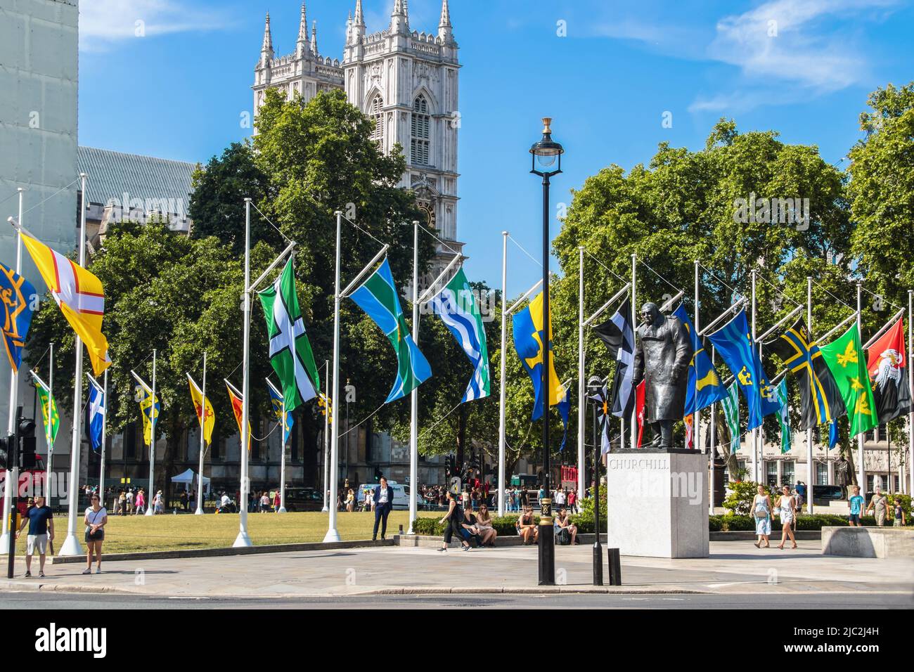 7-24-2019 London UK - Statue von Winston Churchill auf dem Parliament Square mit den Flaggen der Kronenabhängigkeiten und der Überseegebiete, die auf der Sonne fliegen Stockfoto