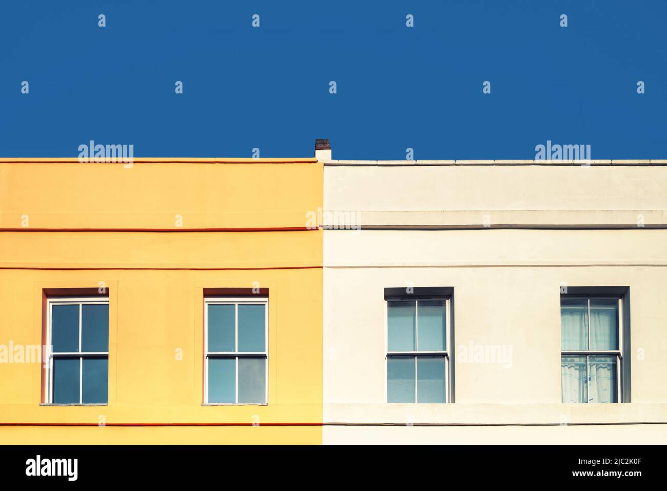 Gelbes Haus, weißes Haus und blauer Himmel. Minimalistischer Stil mit Platz für Text. Geometrisches Fenster und Details der Fensterfront Stockfoto