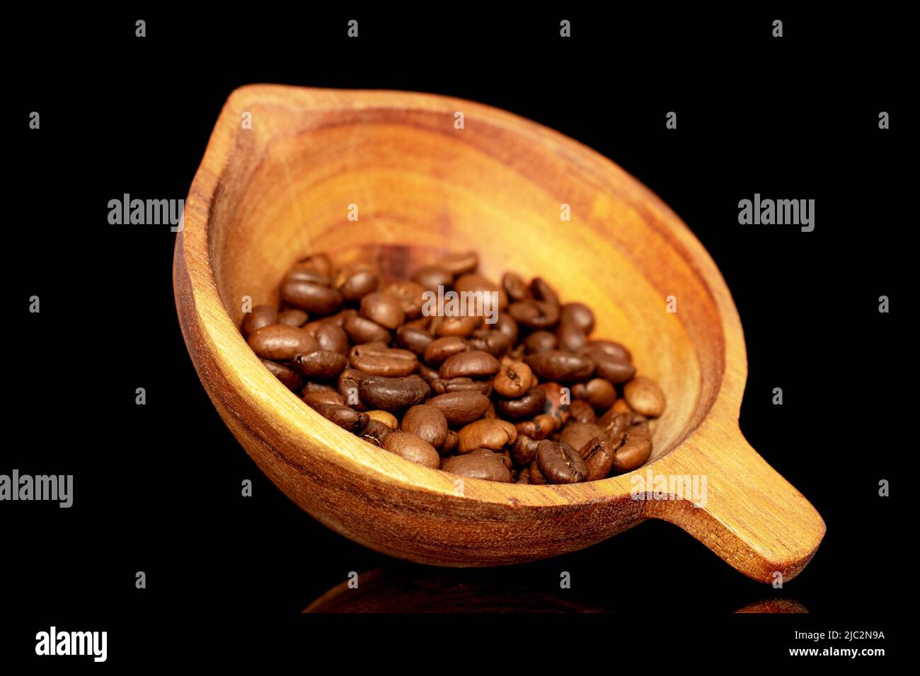 Geröstete aromatische Kaffeebohnen in einer Holztasse, Nahaufnahme, isoliert auf schwarzem Hintergrund. Stockfoto