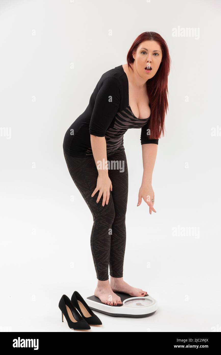 Wiltshire, England, Großbritannien. 2022. Eine überraschte Frau, die ein Set von Badezimmerwaagen benutzt, um ihr Gewicht zu überprüfen. Stockfoto