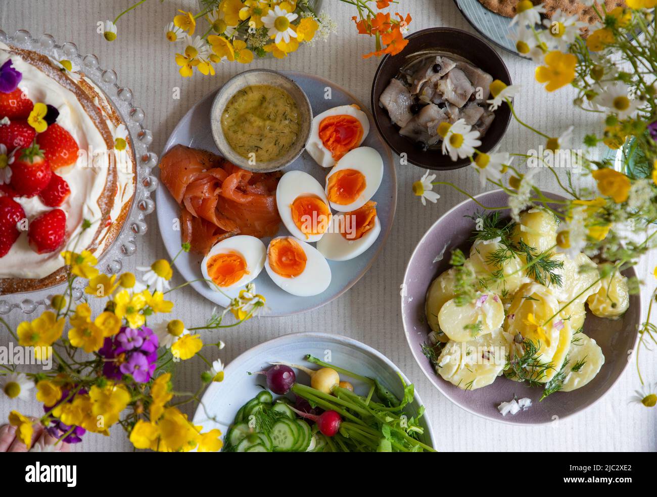 Skandinavisches Mittsommergericht mit Erdbeer- und Cremekuchen, Kartoffelsalat, Lachs und Eiern Stockfoto