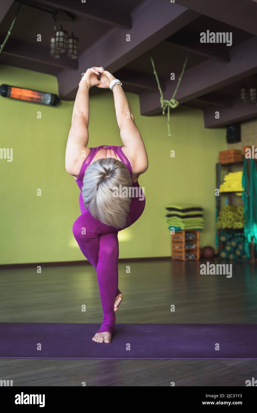 Eine Frau, die Yoga praktiziert, führt eine Variante der garudasana-Übung durch, der Adler posiert mit den Armen hinter ihrem Rücken, steht auf einer Matte im Raum Stockfoto