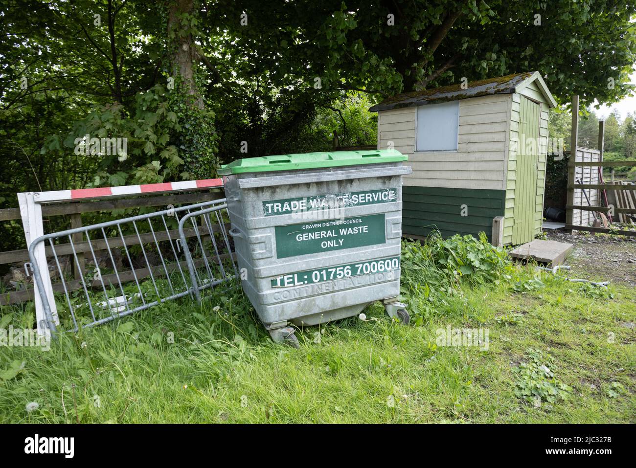 Abfallbehälter, der im Gras vor einem kleinen Zaun steht Stockfoto