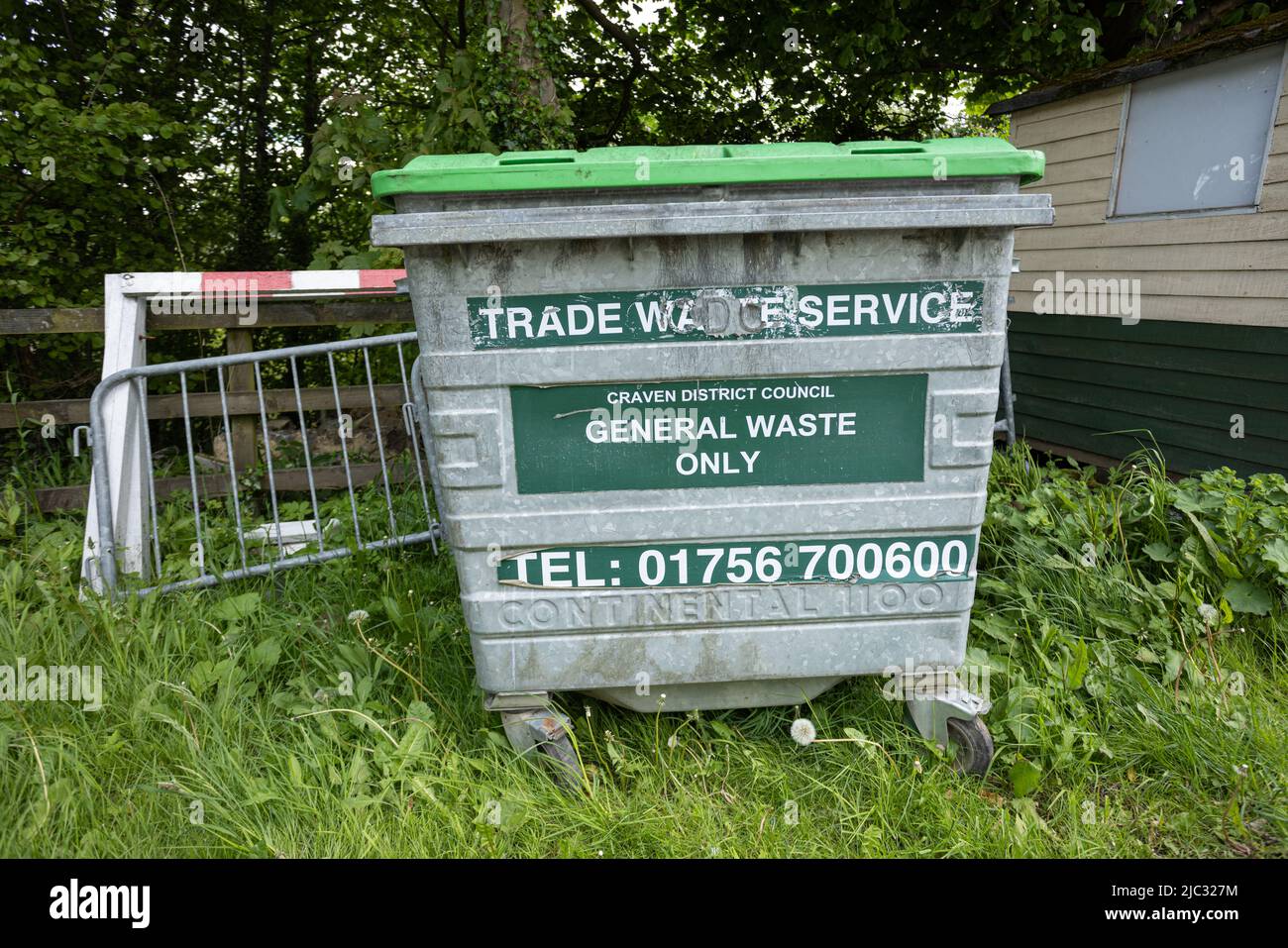 Abfallbehälter mit grünem Deckel, der im Gras vor einem kleinen Zaun steht Stockfoto