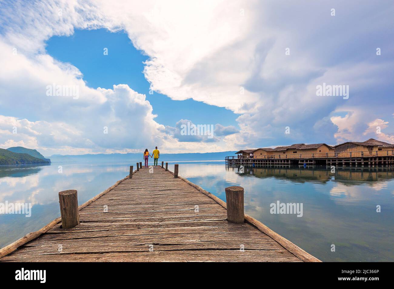 Hölzerner Pier und Wolkenlandschaft mit einem Paar am Ende des Docks in der Bucht, die als Knochenbucht im Ohridsee, Mazedonien, bekannt ist. Stockfoto