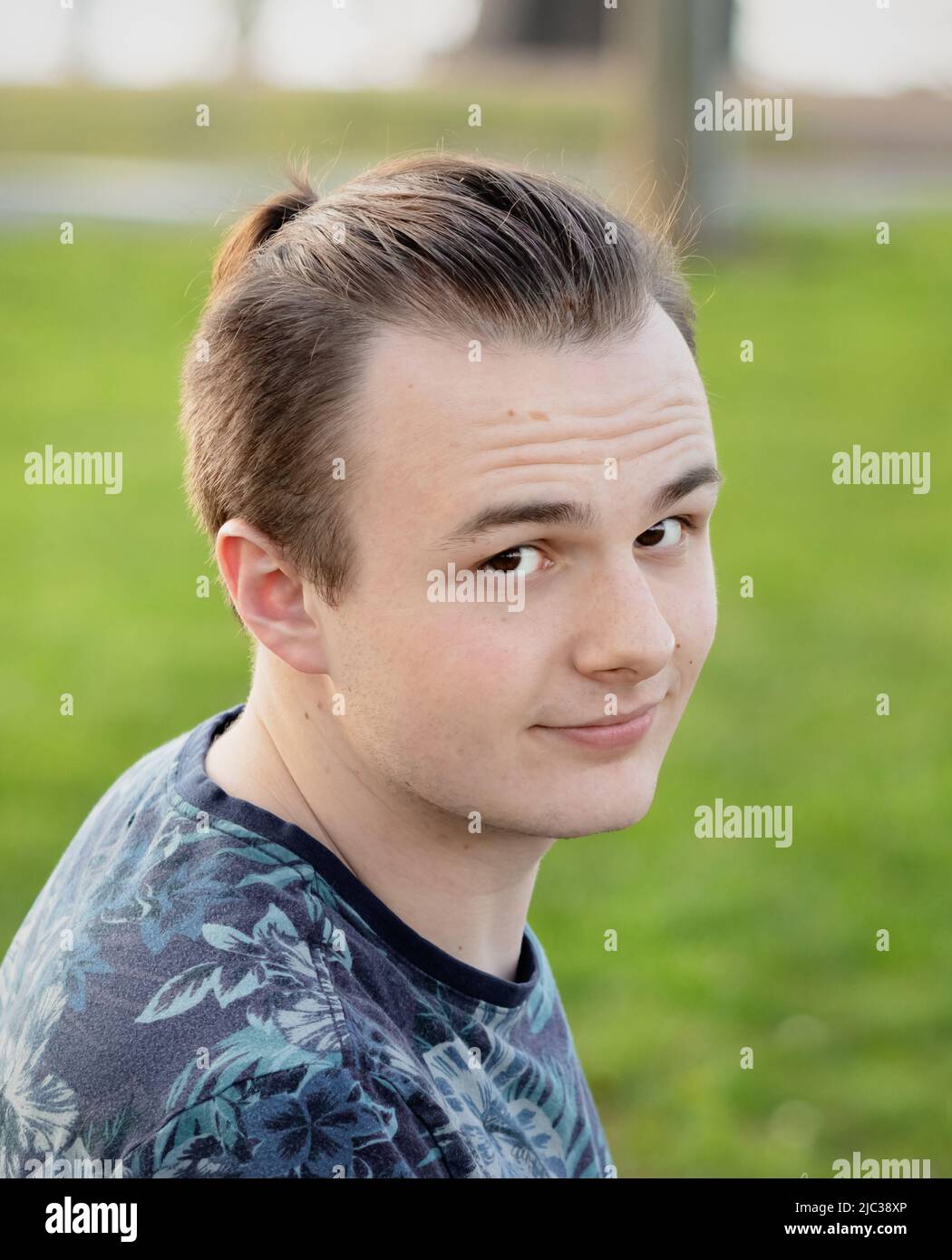 Junger erwachsener Mann mit braunen Augen und braunen Haaren in einem Park und Blick auf die Kamera mit grünem Gras im Hintergrund, Lancaster, Pennsylvania Stockfoto
