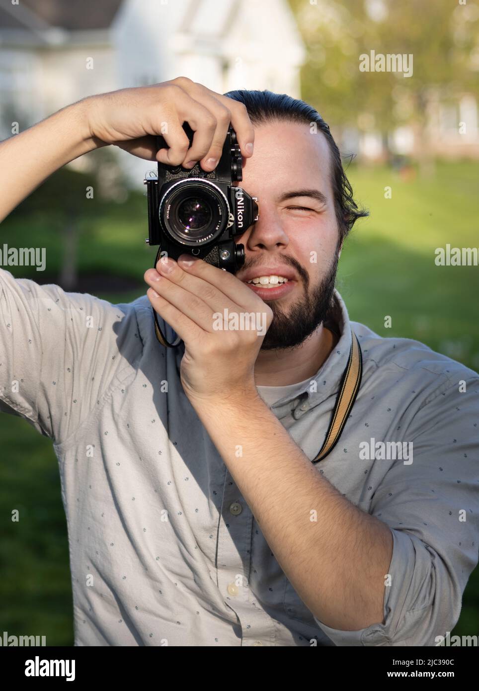 Ein bärtiger junger erwachsener Mann mit Kamera zeigte auf den Betrachter, der im Frühjahr oder Sommer ein Foto in einem Park in Lancaster, Pennsylvania, machte Stockfoto