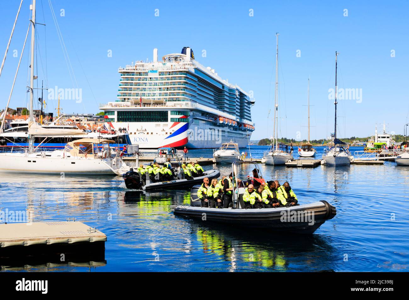 Touristen besetzen aufblasbare Boote für eine schnelle Fahrt auf den Fjorden. Alle sind in Hi-viz Jacken. P & O Cruises MS Iona liegt an den Kais Stockfoto