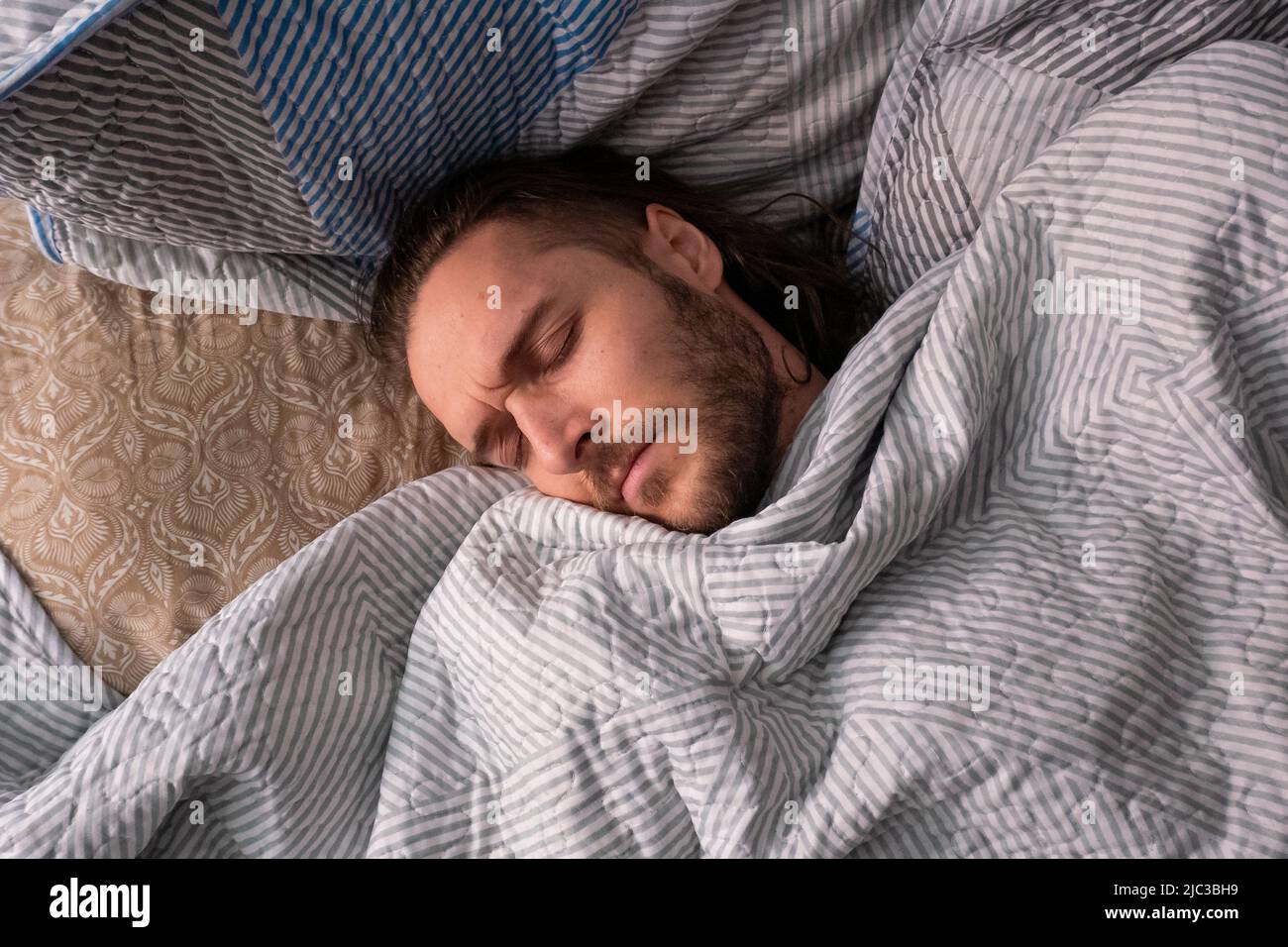 Weißer Mann schläft im Bett mit einem Haufen Kissen Stockfoto