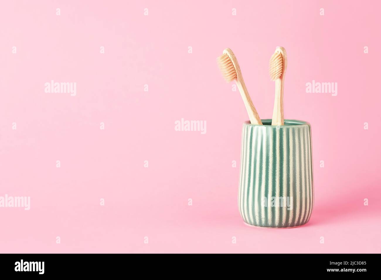 Zwei Bambus-Zahnbürsten in einem grünen Keramikhalter auf einem rosa Hintergrund. Umweltfreundliches, abfallfreundliches Konzept. Platz für Text kopieren, selektiver Fokus Stockfoto