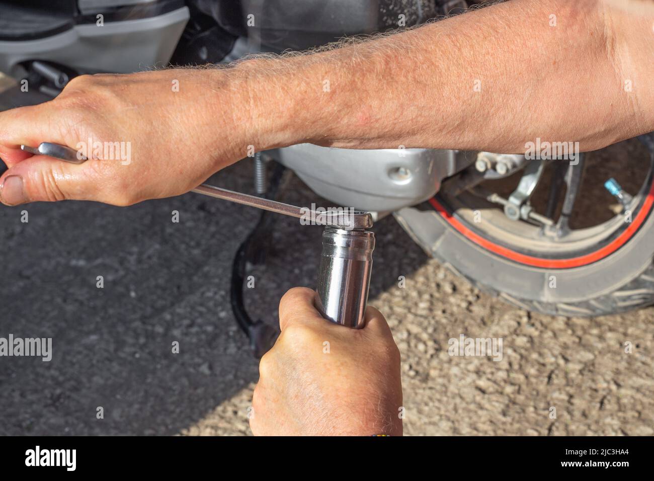 Wartung und Reparatur von Motorrädern. Ein Automechaniker verwendet einen Schraubenschlüssel, um den Stopfen am Stoßdämpfer der Vorderradgabel eines Motorrollers festzuziehen. Stockfoto