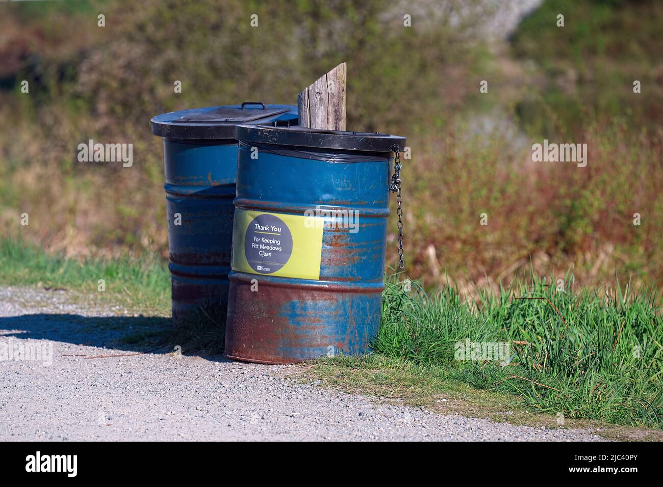 Blaue Metallabfallbehälter, die an einen Pfosten entlang eines Erholungsweges gekettet werden. Stockfoto