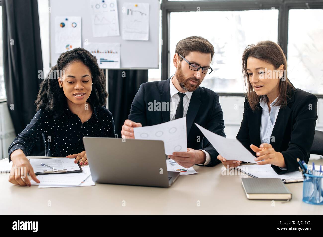 Multirassische kreative Kollegen führen gemeinsam Brainstorming zu einem neuen Start-up durch, sitzen im modernen Büro, studieren Dokumente, nutzen Laptops und diskutieren den Finanzgeschäftsplan. Konzept der Teamzusammenarbeit Stockfoto