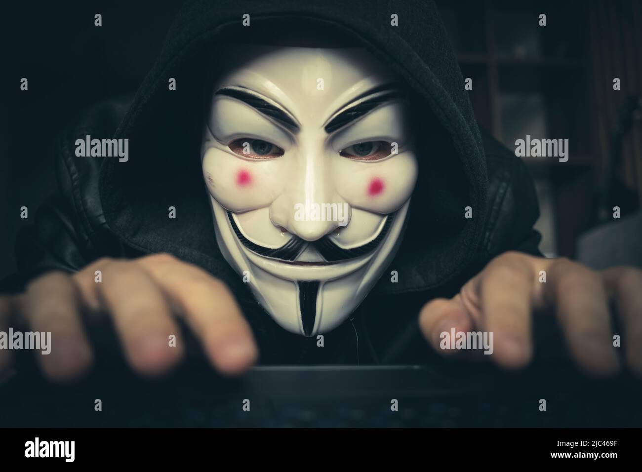 Hacker-Cracker mit anonymer Assoziationsmaske, die auf dem Laptop arbeitet. Anonymous ist ein locker verbundes internationales Netzwerk von Aktivisten und Hacktivi Stockfoto