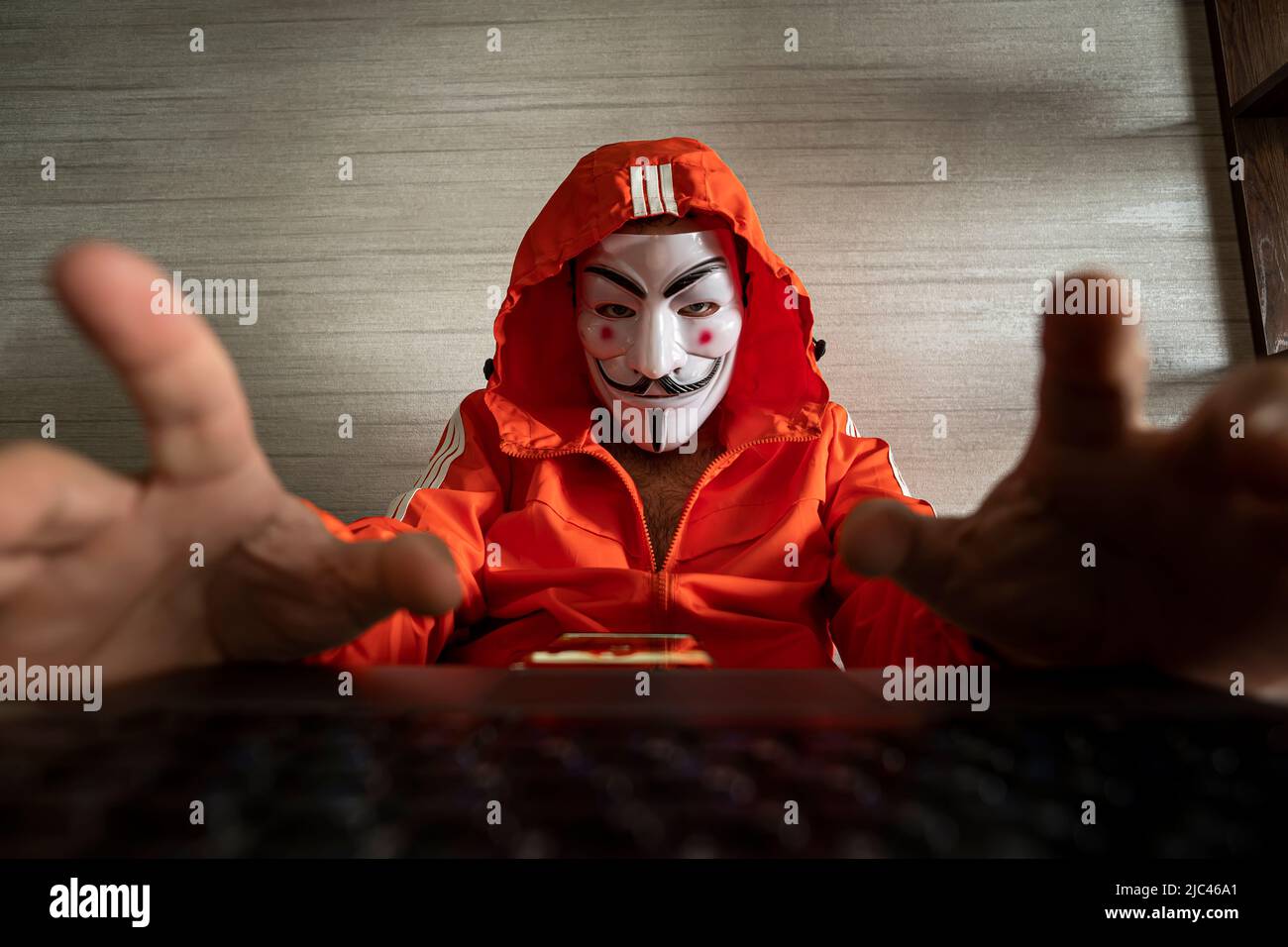 Hacker-Cracker mit anonymer Assoziationsmaske, die auf dem Laptop arbeitet. Anonymous ist ein locker verbundes internationales Netzwerk von Aktivisten und Hacktivi Stockfoto