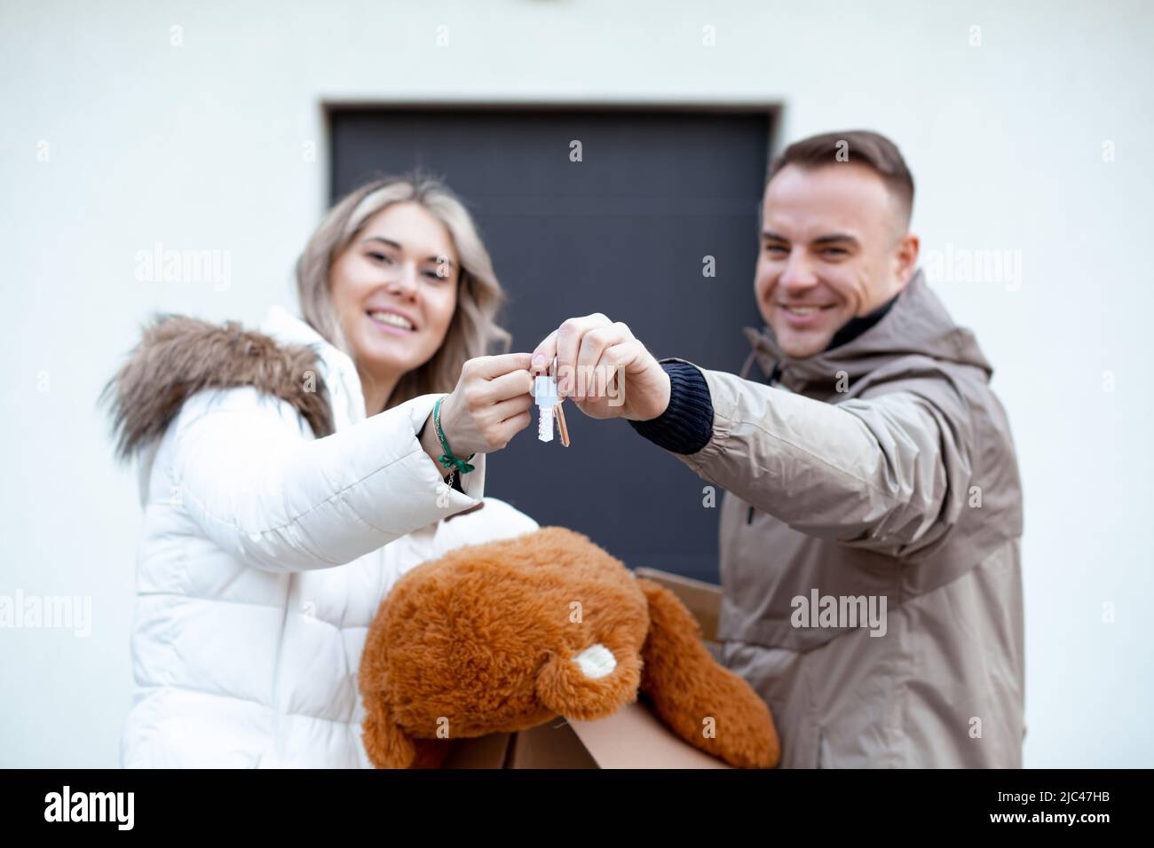 Porträt einer jungen, lächelnden, glücklichen Familie, Frau und Mann, die die Schlüssel vor der Kamera halten und sich in das neue Haus vor der Tür bewegen Stockfoto